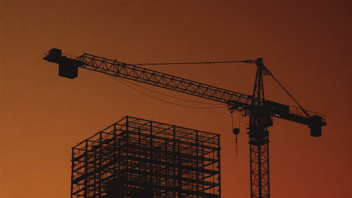 Steel frame and tower crane against a burnt-orange dusk sky